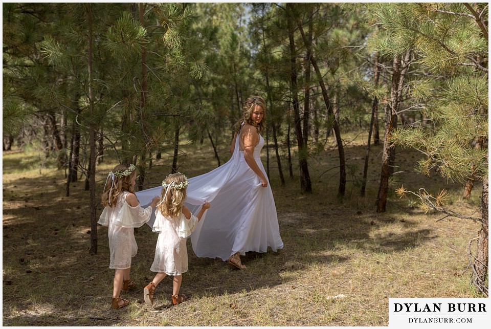 boho backyard colorado wedding bride walking in forest with daughters holding dress