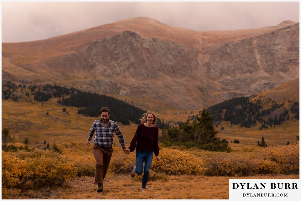 fall engagement photos in colorado couple running in mountain meadow