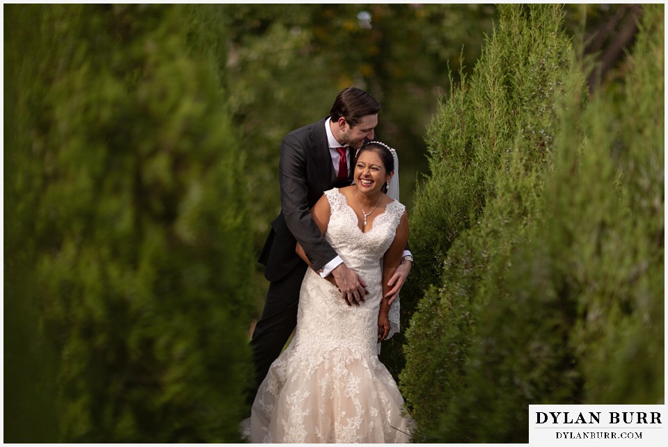 baldoria on the water wedding lakewood colorado hindu wedding bride and groom in tall juniper trees laughing