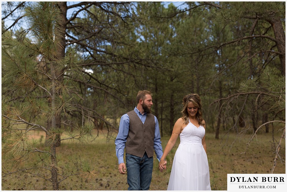 boho backyard colorado wedding bride and groom walking in forest holding hands