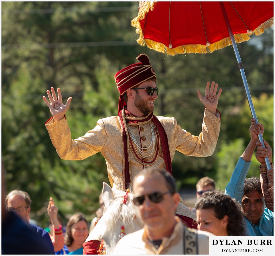 cielo at castle pines wedding colorado mountain wedding groom on horse with henna on hands during hindu wedding barat