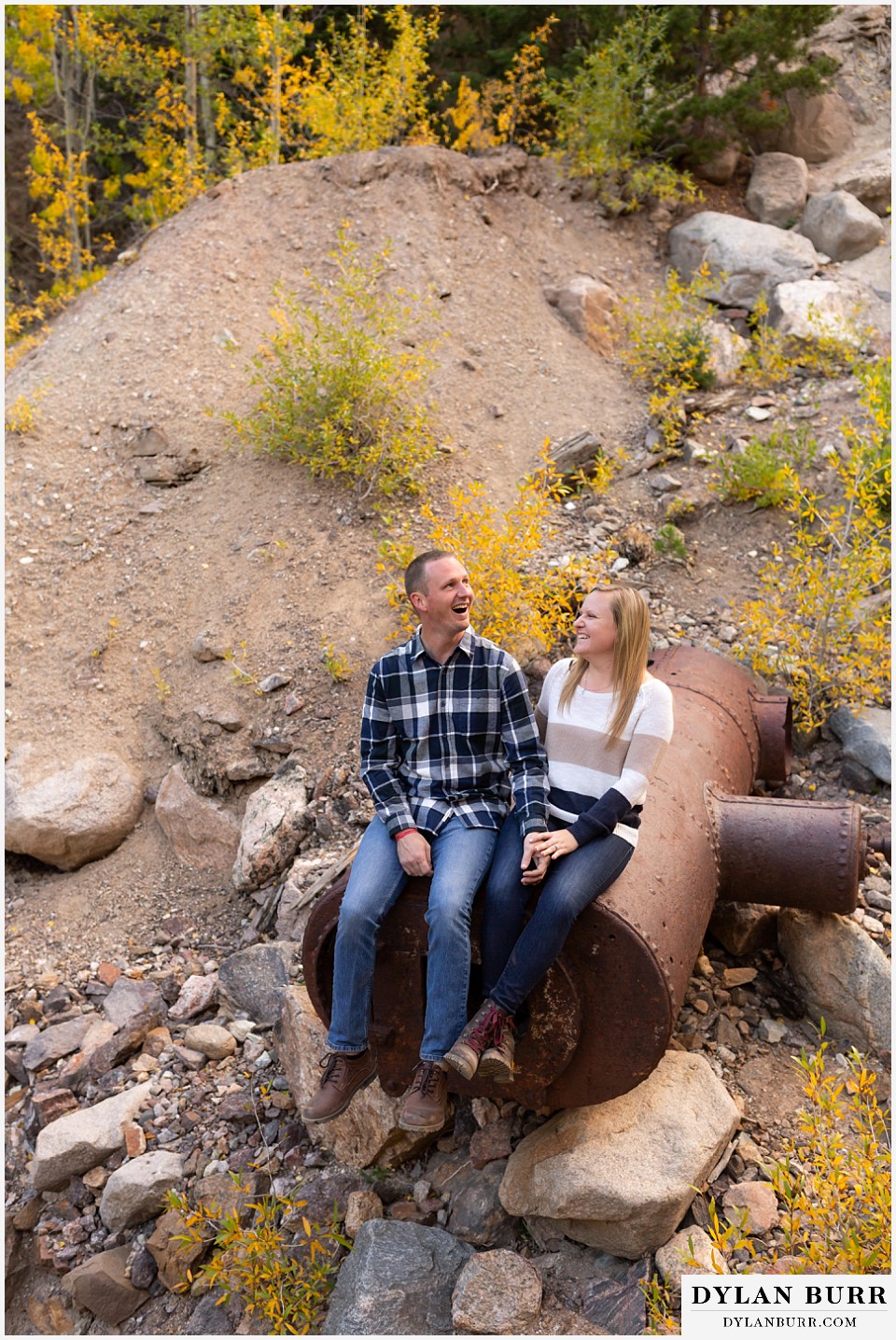 engagement photos in colorado couple sitting on old mining equiptment and laughing