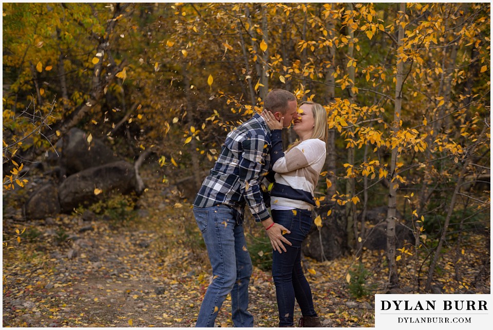 engagement photos in colorado couple coming together with fall leaves falling