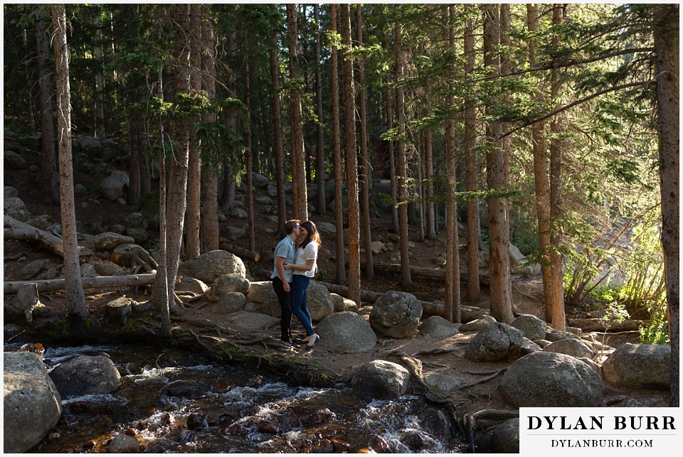 colorado mountain engagement photos colorado wedding photographer dylan burr wide view of couple near river in pine tree forest