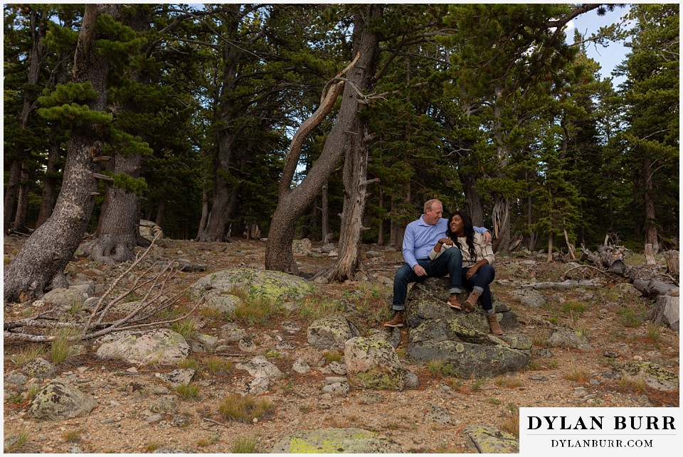 colorado mountain engagement photos couple sitting on rock in windblown pine trees