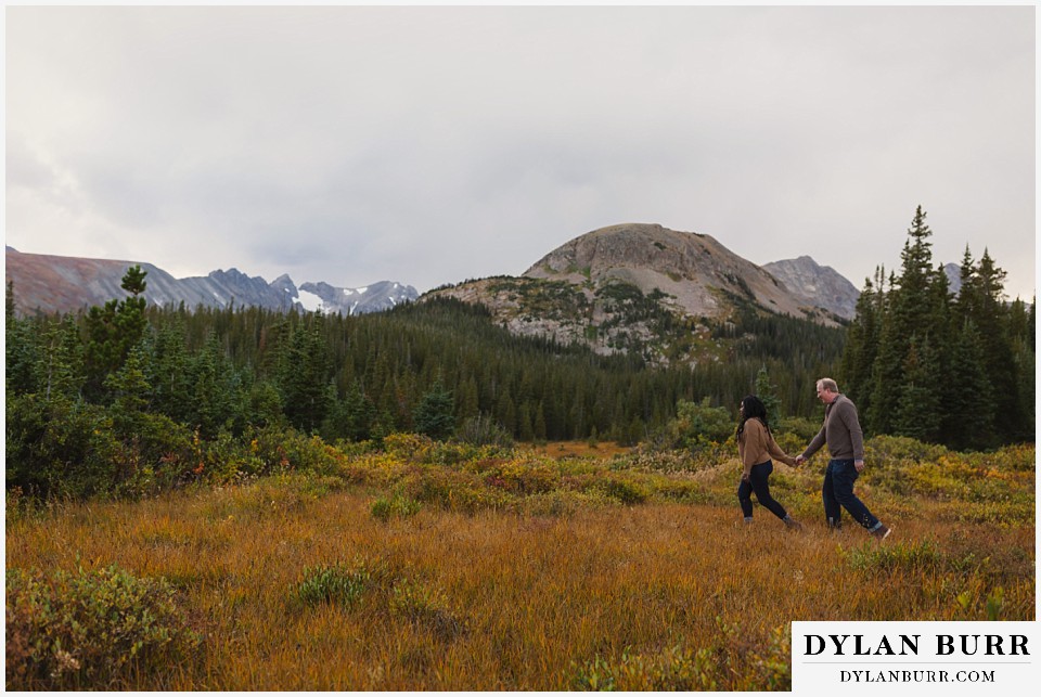 colorado mountain engagement photos couple walking across mountain meadow in fall