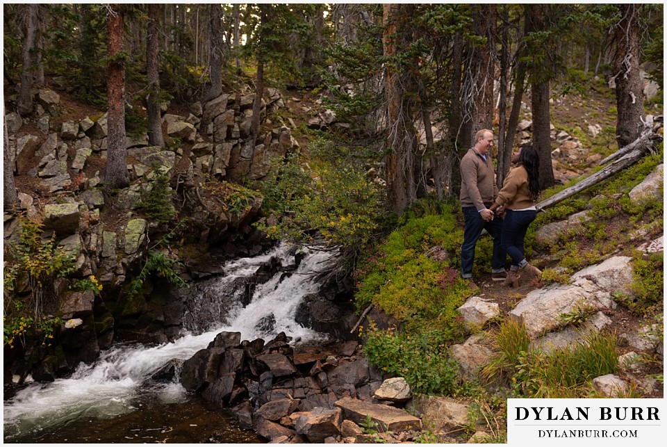 colorado mountain engagement photos couple standing together in forest by waterfall