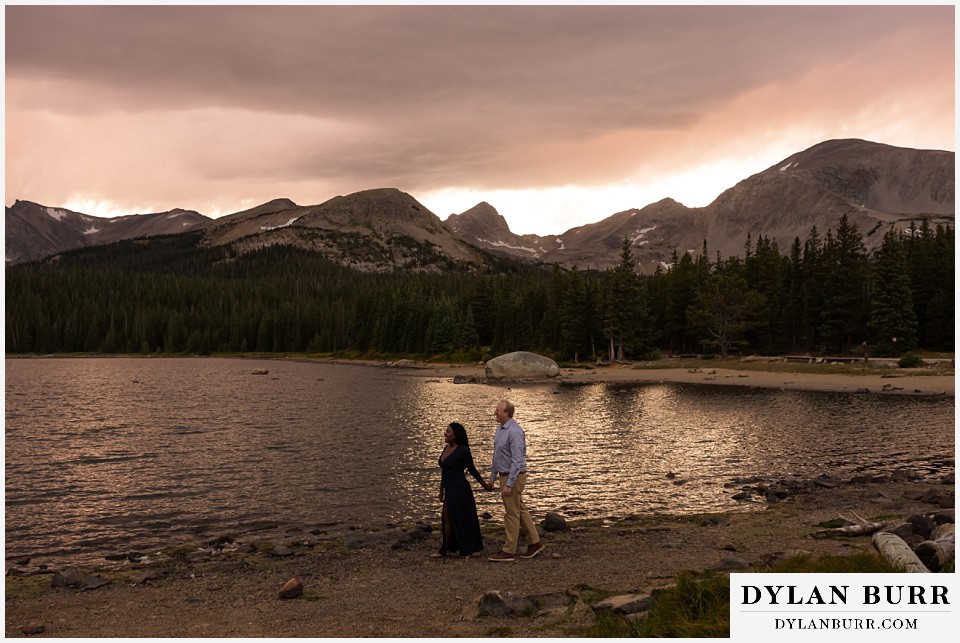 colorado mountain engagement photos couple walking together by mountain lake at sunset