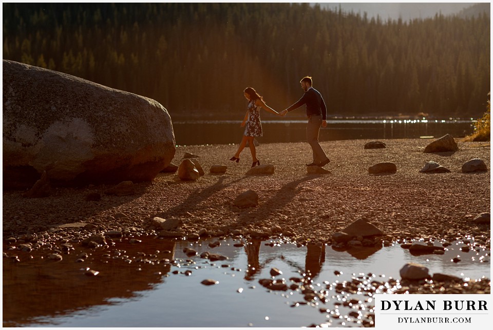 colorado engagement photos in mountains couple walking out on stepping stones in lake