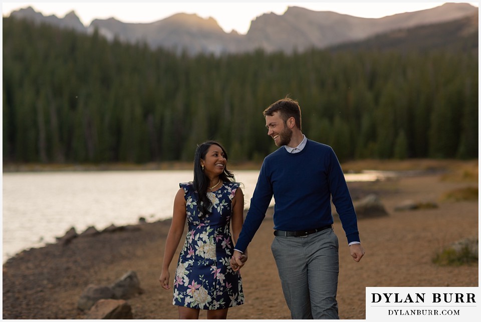 colorado engagement photos in mountains couple walking along lake and laughing