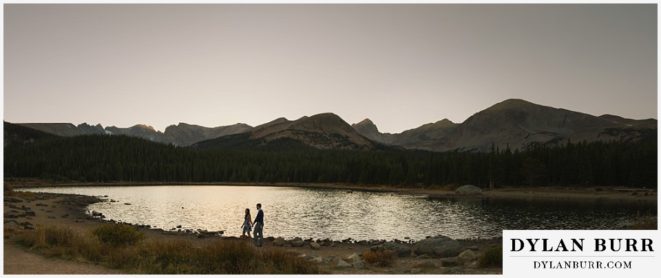 colorado engagement photos in mountains walking along lake shore at dusk