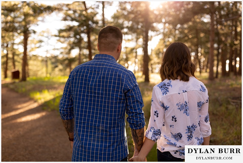 golden colorado mountain enagagement photo session couple walking into sunlit field in pine forest