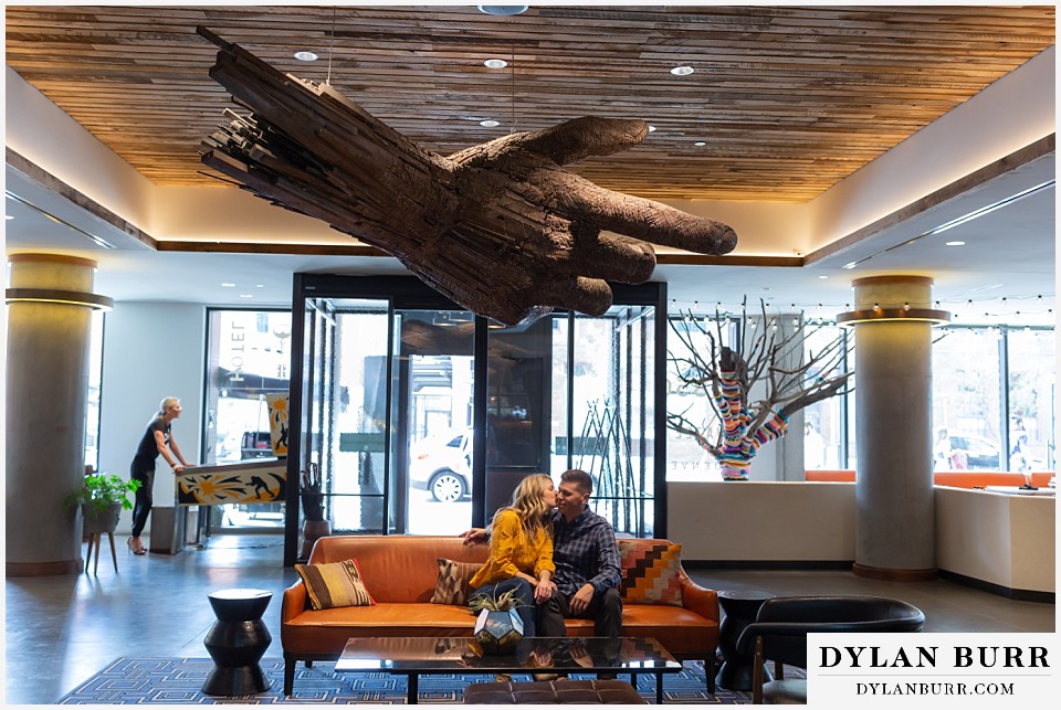 denver engagement photos dairy block downtown denver sitting together under large art hand sculpture