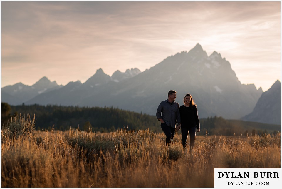 grand teton wedding anniversary photos couple holding hands in field by giant mountains