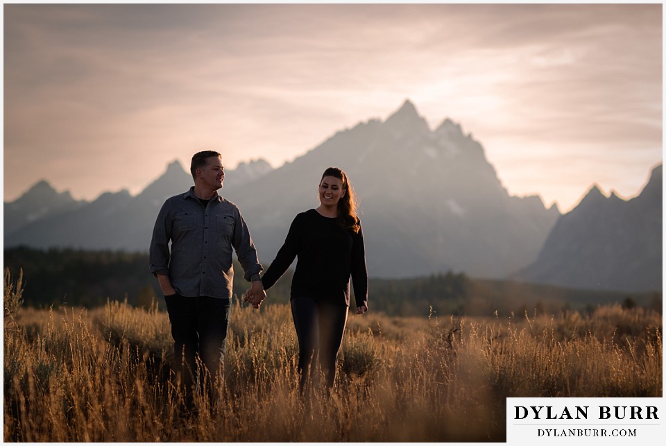 grand teton wedding anniversary photos couple walking as he leads giant mountains in distance