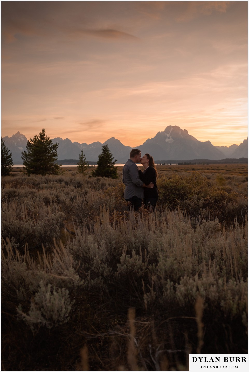 grand teton wedding anniversary photos standing in tall sagebrush with grand teton mountains in the distance at sunset