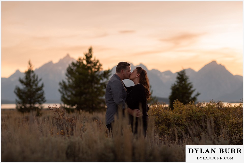 grand teton wedding anniversary photos couple kisses in front of mountains at sunset
