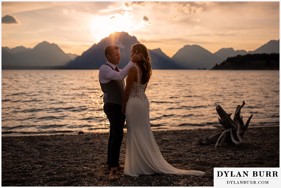 jackson lake lodge wedding grand tetons wyoming groom brushing brides hair back near jackson lake and mt moran