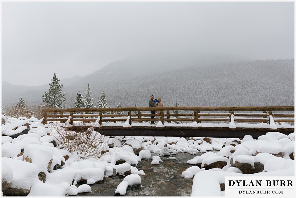 wedding proposal standing on a bridge over a river in snowy foggy weather