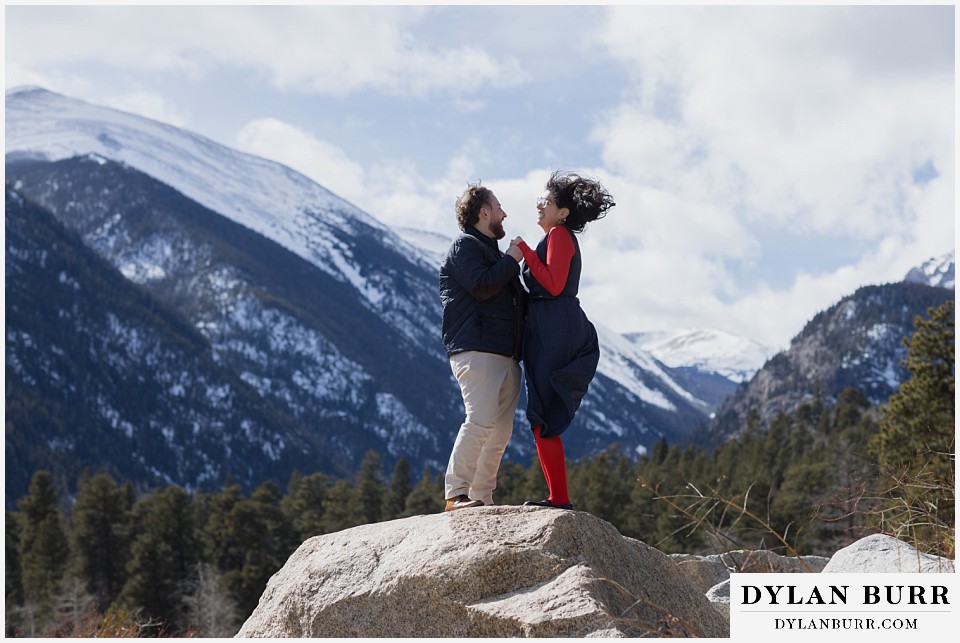 engaged couple standing together on a rock in the crazy wind