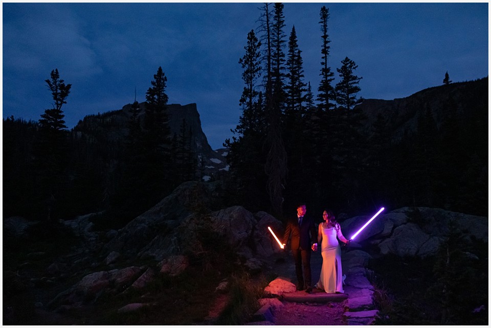 sunrise hike elopement to dream lake couple holding lightsabers on the trail