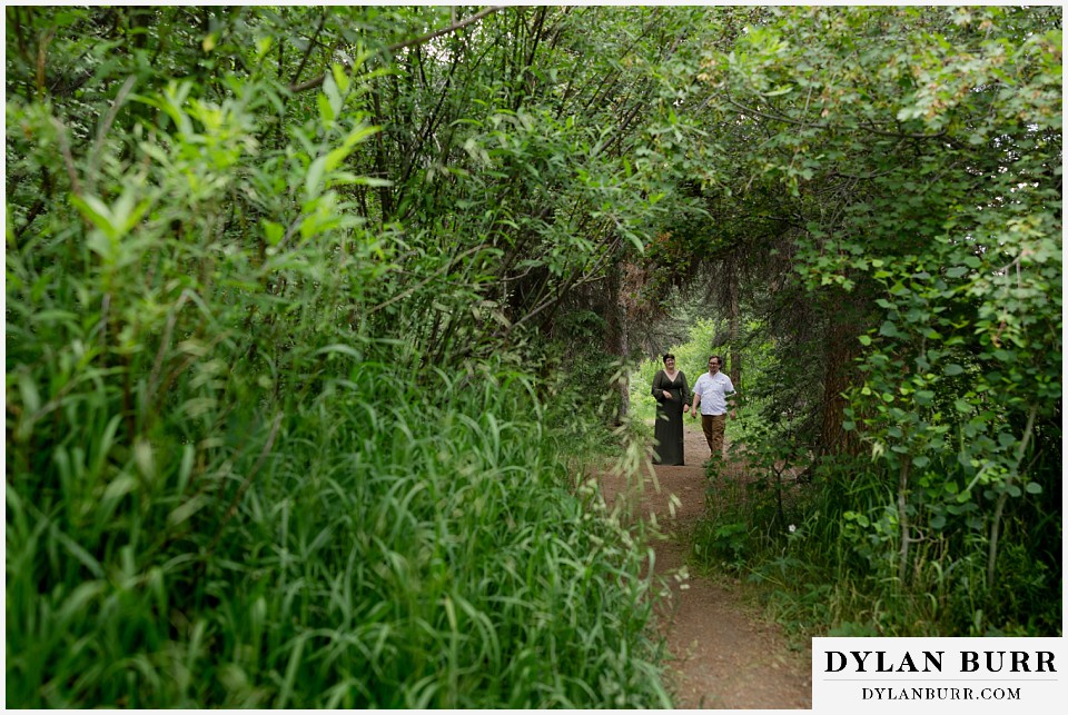 water engagement session rocky mountain national park couple walking down tree lined trail together