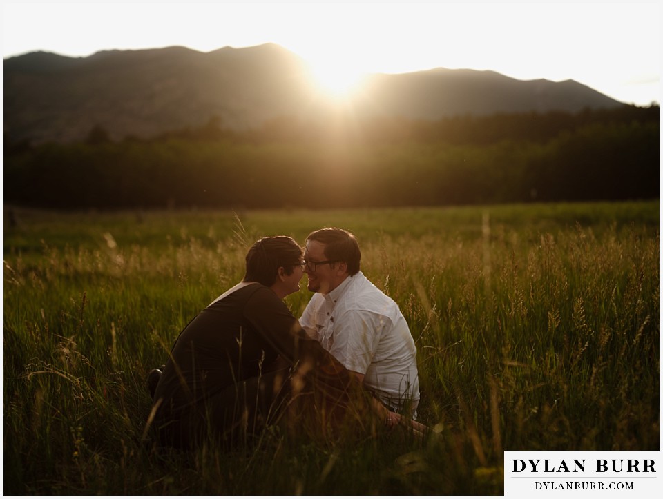 water engagement session rocky mountain national park kissing in a grassy meadow as the sun goes down