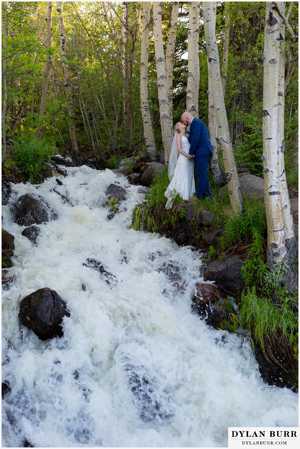 bride and groom kissing near large river in mountains with aspen trees